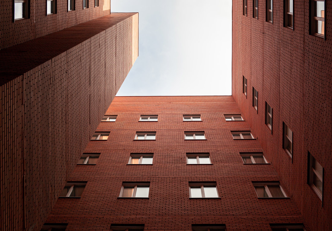 View looking up towards the sky between two tall brick buildings with multiple rectangular windows.