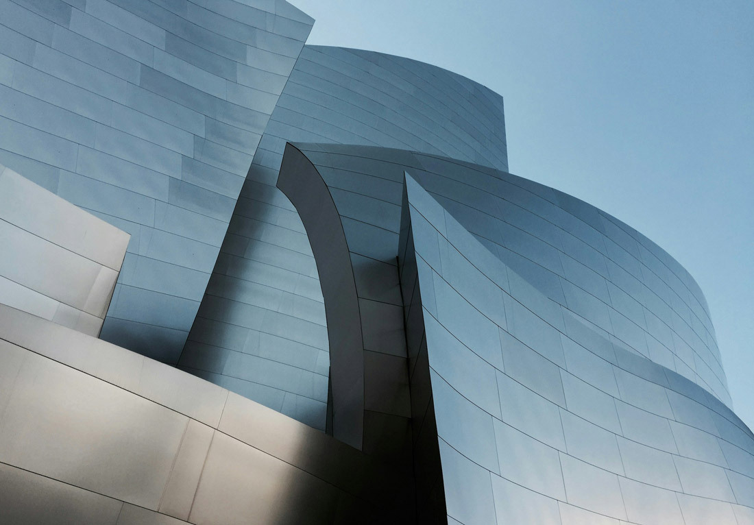 Modern architectural structure with smooth, metallic panels forming abstract curves against a blue sky.
