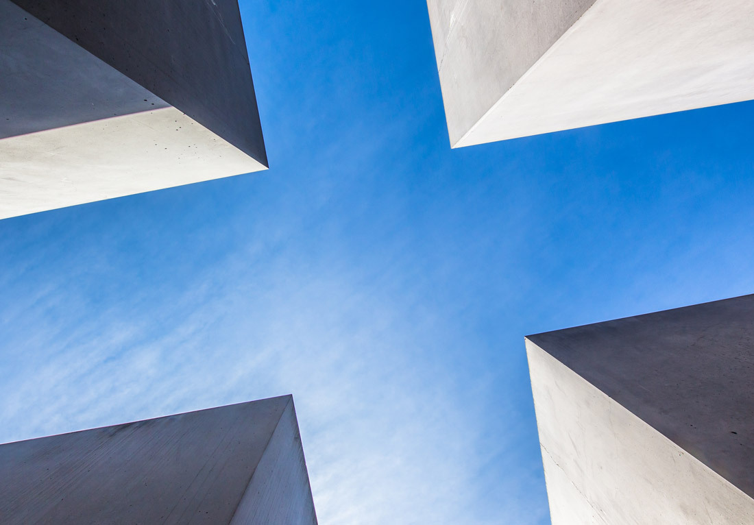 View from below of four large, concrete slabs arranged in a cross formation against a clear blue sky.