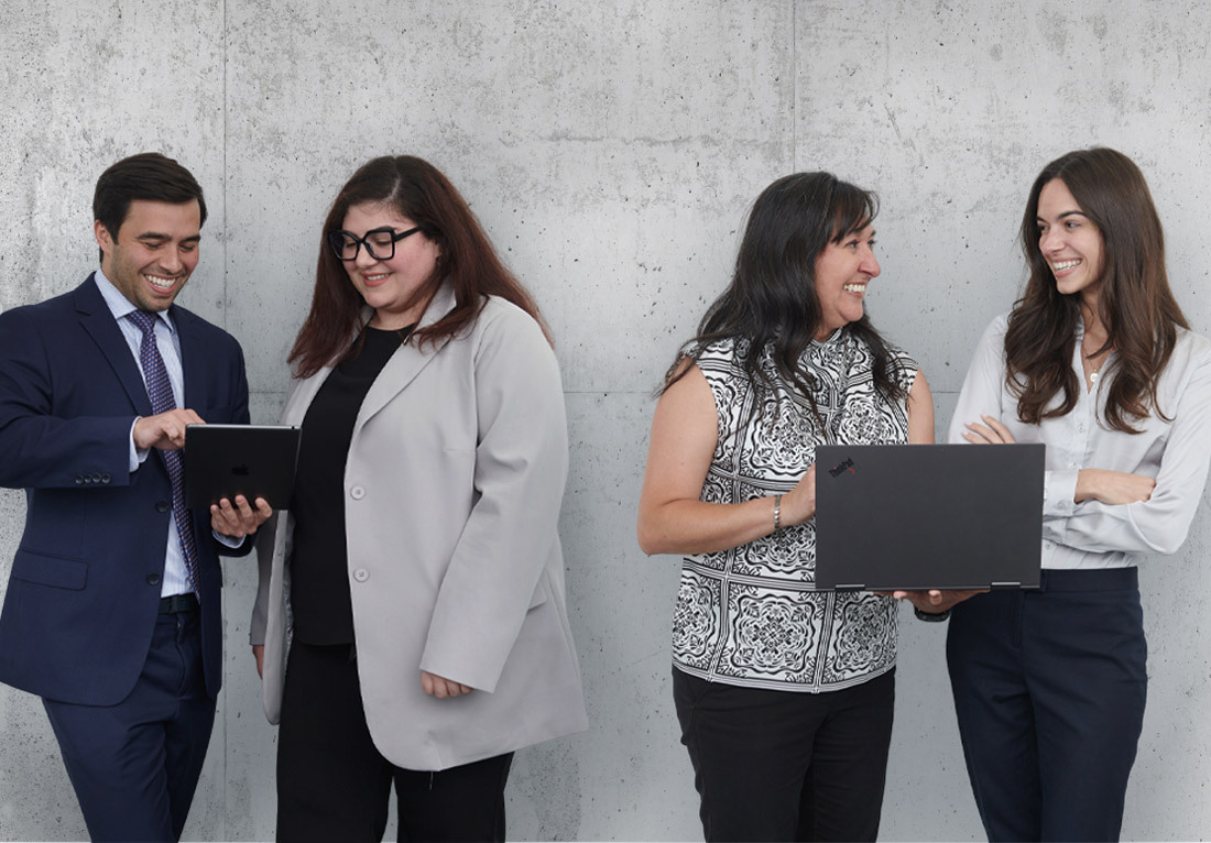 Group of four professionals from Koley Jessen standing against a textured gray wall, dressed in business attire. One individual holds a tablet, another holds a laptop.